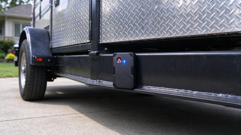A magnetic GPS tracker attached to the painted steel frame of a parked utility trailer
